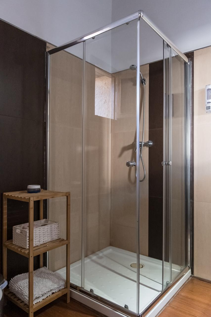 Corner shower cabin with a wooden shelf rack alongside.