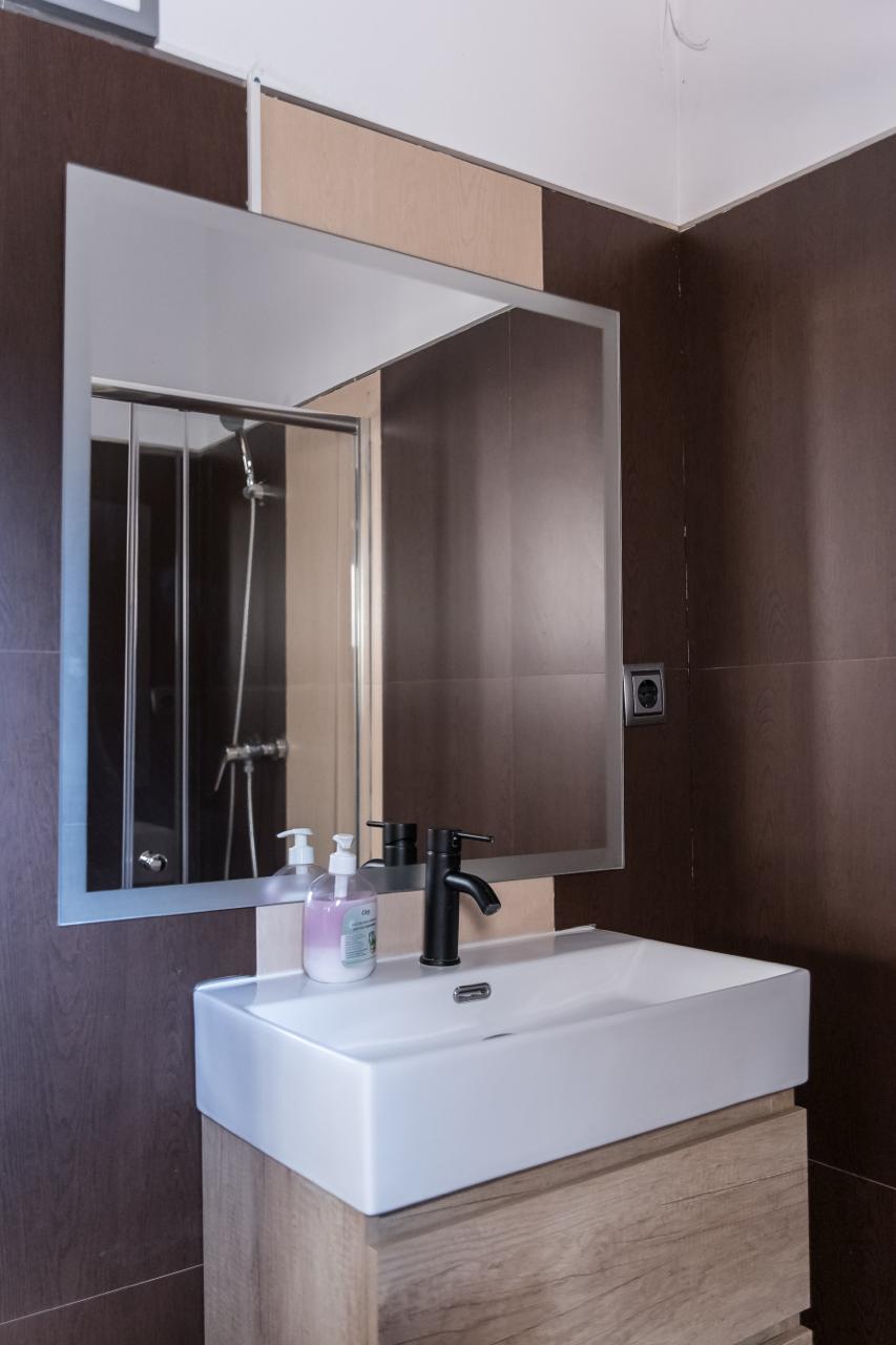 Bathroom with dark brown tiling, basin and mirror.