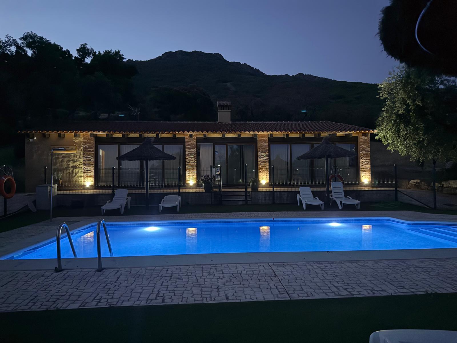 The pool lit blue at dusk, the pavilion facade uplit behind it.