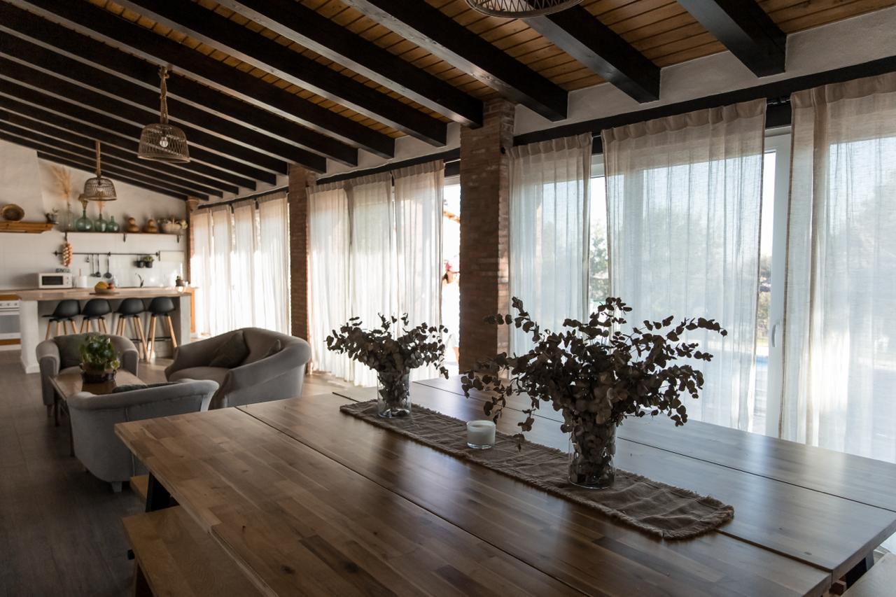 The pavilion's long dining table with dried flowers, light filtering through full-height linen curtains.