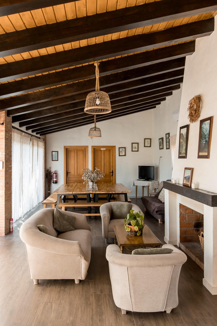 Inside the dining pavilion: armchairs around a low table, a long dining table beyond, and an open fireplace to the right.